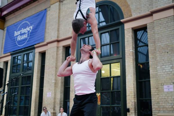 two male circus performers. One is doing a handstand on the other's hands 