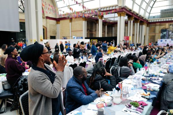 people around tables and clapping in a large performance scape 