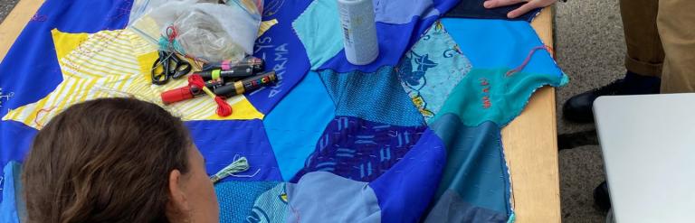 two people adding to a blue patchwork quilt